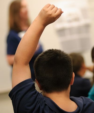 Child raising hand in classroom.